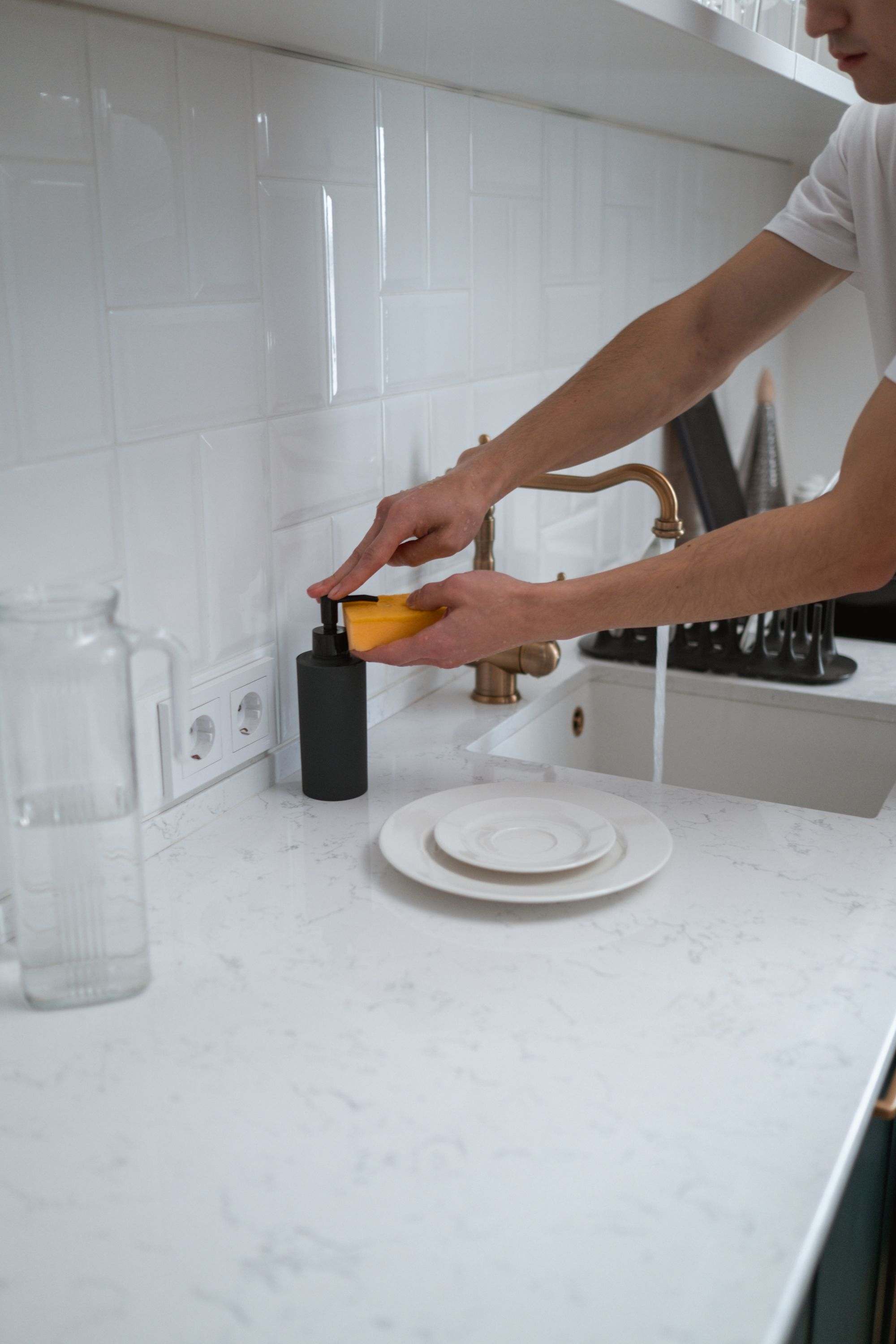 Hands rinsing a white plate at a spotless marble countertop sink